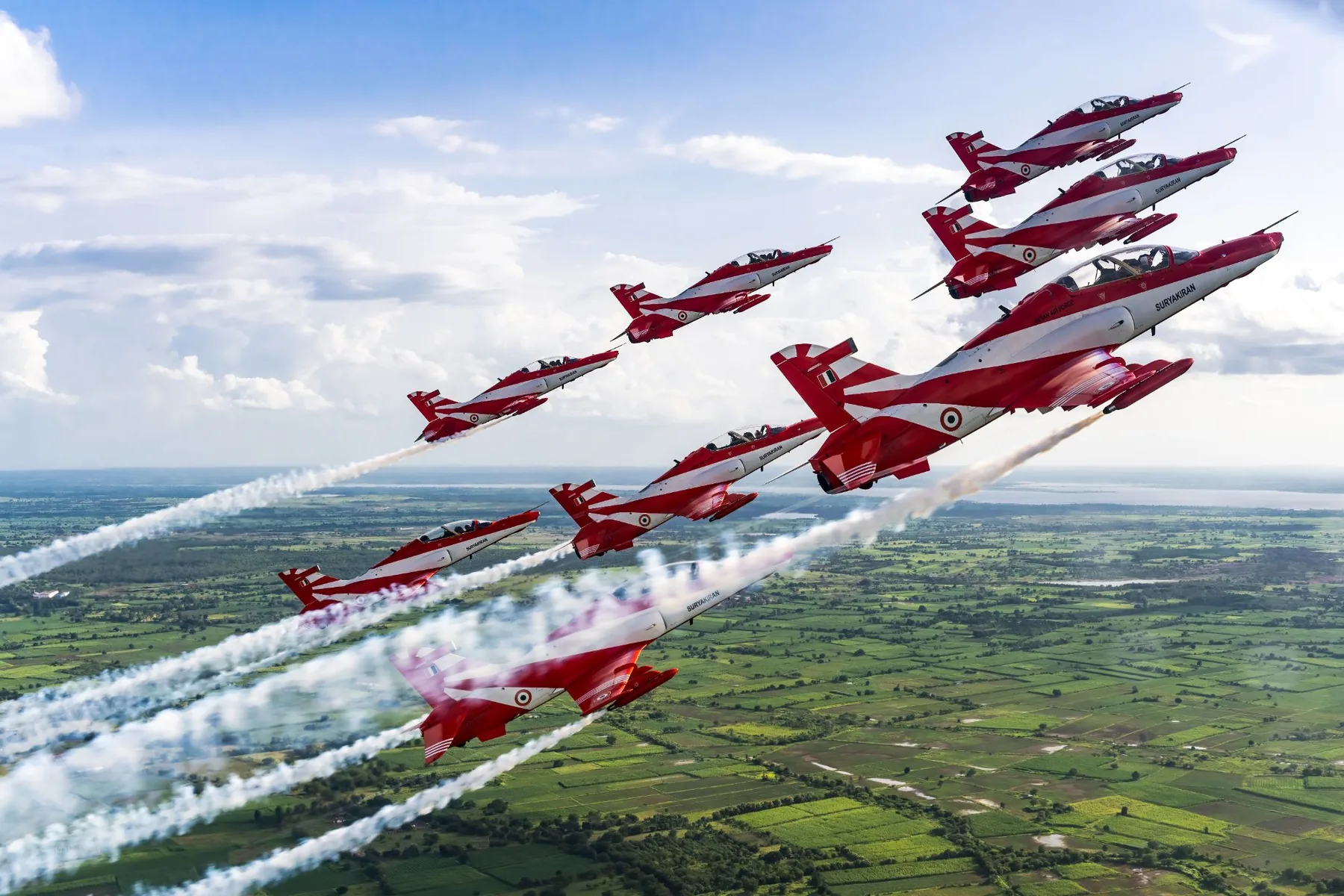 The Suryakiran Aerobatic Team flying in formation over green fields