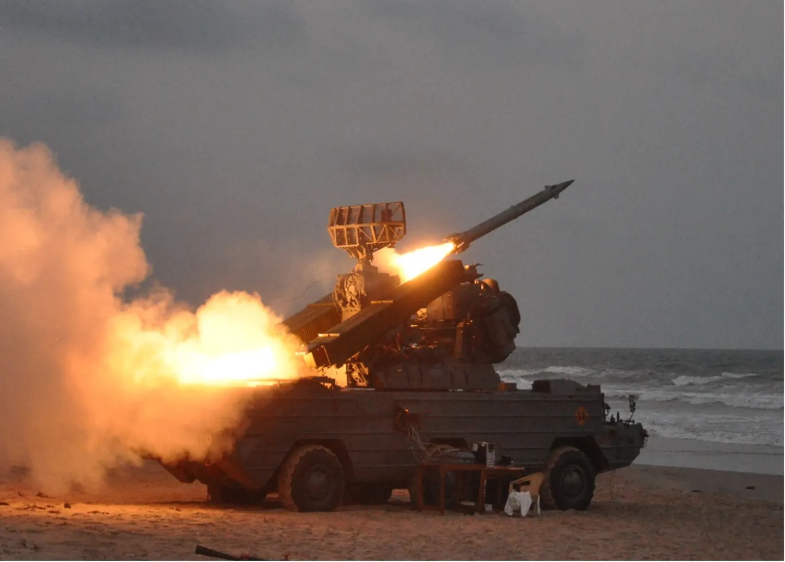 A surface-to-air missile fired from a launcher on a beach at dusk