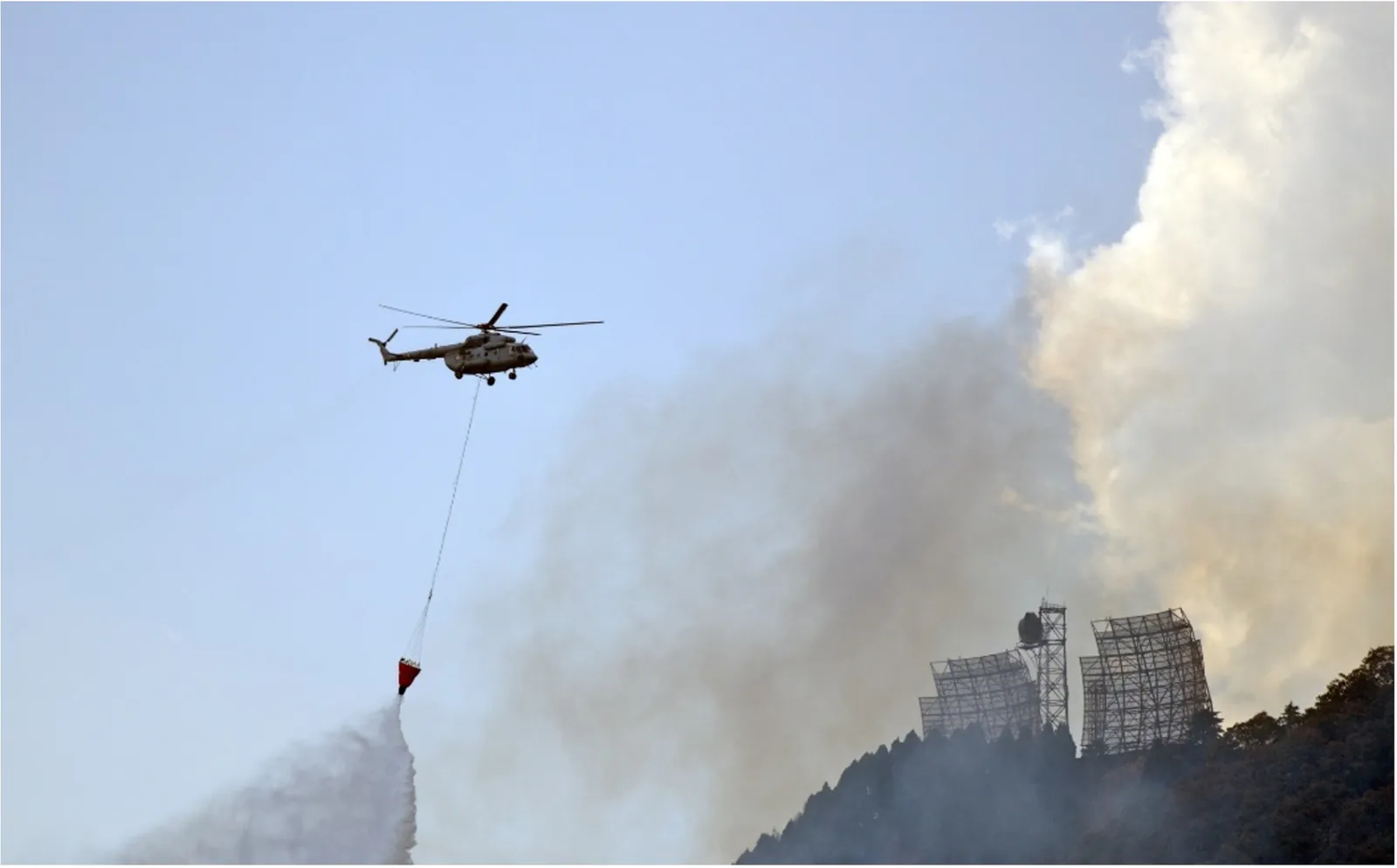 A Mi-17 V5 helicopter carrying a water bucket over a burning hillside